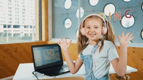 Smiling girl looking at camera while waving hand with laptop placed. Erudition. Stock Photos