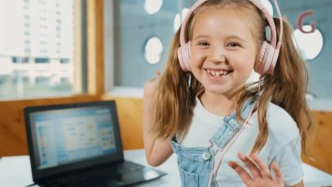 Smiling girl looking at camera while waving hand with laptop placed. Erudition. Stock Photos