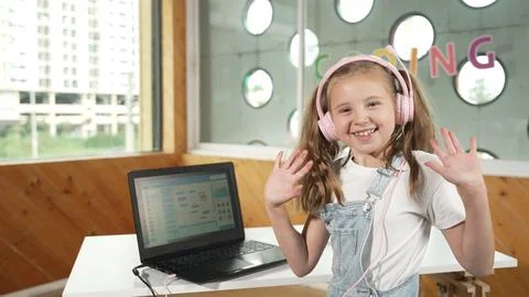 Smiling girl looking at camera while waving hand with laptop placed. Erudition. Stock Photos