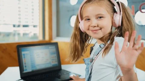 Smiling girl looking at camera while waving hand with laptop placed. Erudition. Stockfoto's