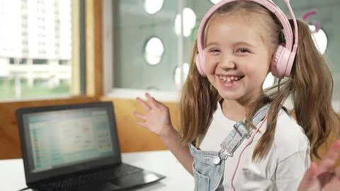 Smiling girl looking at camera while waving hand with laptop placed. Erudition. Stockfoto's
