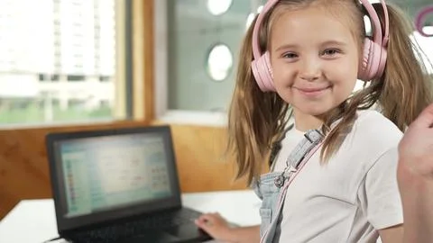 Smiling girl looking at camera while waving hand with laptop placed. Erudition. Stockfoto's