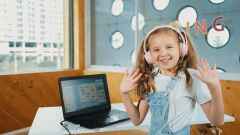 Smiling girl looking at camera while waving hand with laptop placed. Erudition. Stockfoto's