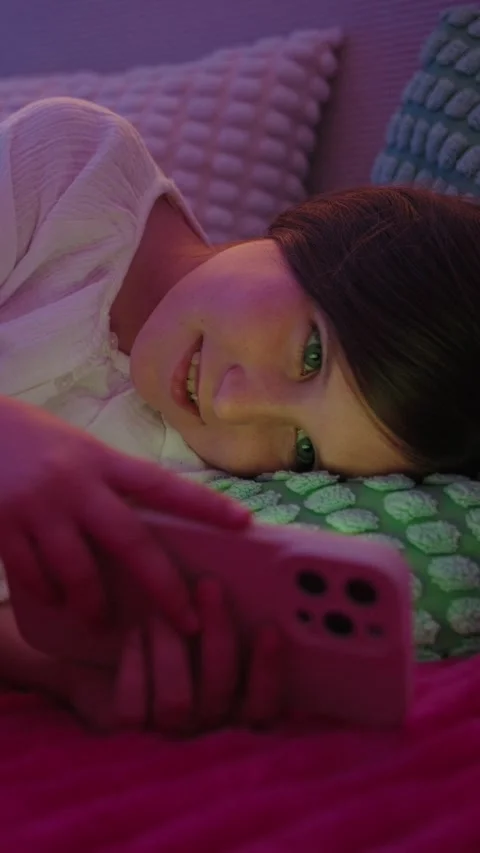 Smiling Girl Lying in Bed Using Smartphone at Night Stock Footage 345528455