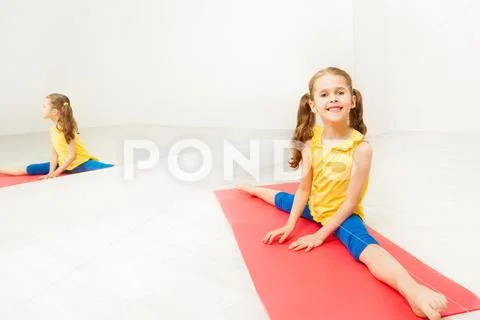 Smiling girl performing side split sitting on mat Stock Photos