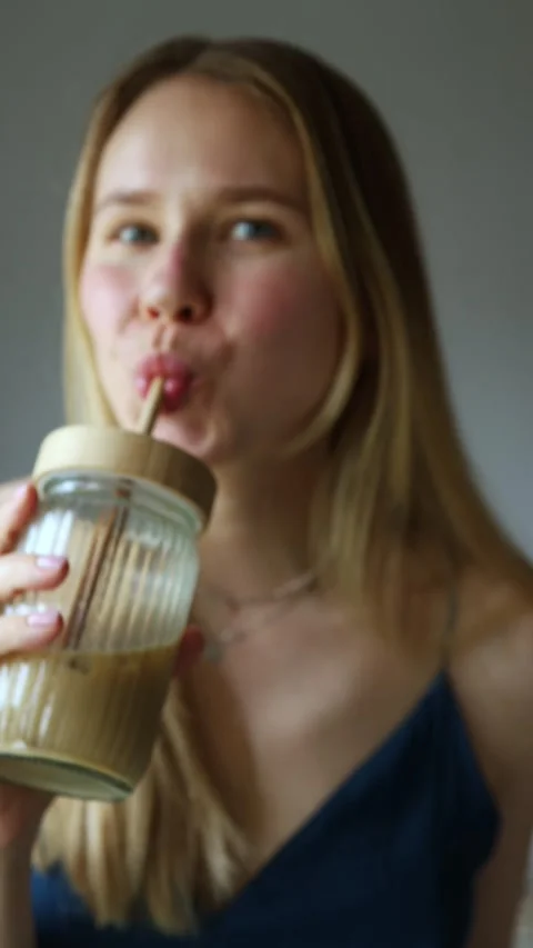Smiling girl playfully dancing while tasting iced coffee through Stock Footage 310608608