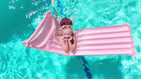 Smiling girl resting on pink float in pool on a sunny summer day 動画素材 312652459