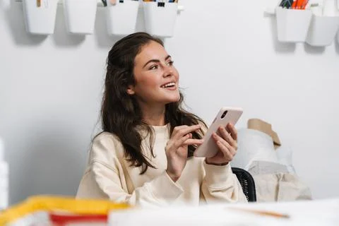 Smiling girl seamstress using mobile phone while working in atelier Stock Photos