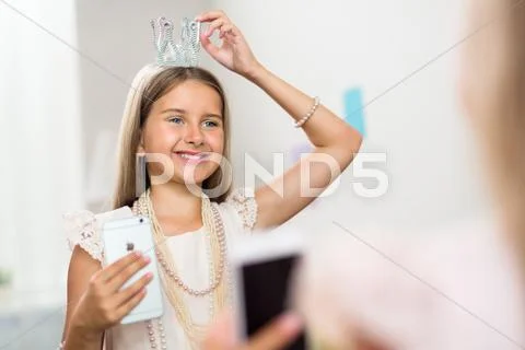 Smiling girl trying little crown on her head in front of mirror Stock Photos