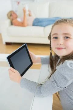 Smiling girl using tablet computer while mother is reading the newspaper Stock Photos