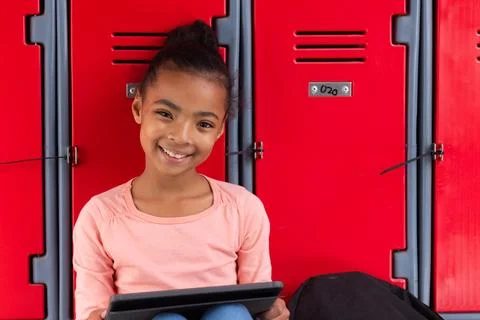 Smiling girl using tablet while sitting in front of red school lockers 스톡 사진
