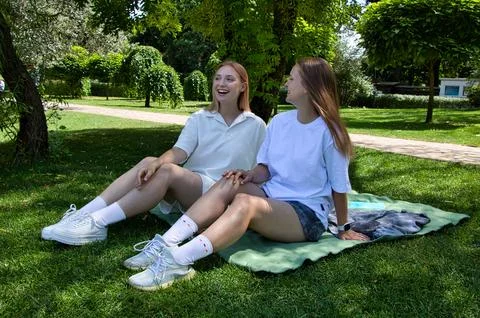 Smiling girls having fun while sitting on a blanket in the park. Stock Photos