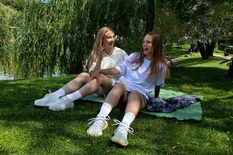 Smiling girls having fun while sitting on a blanket in the park. Stock Photos