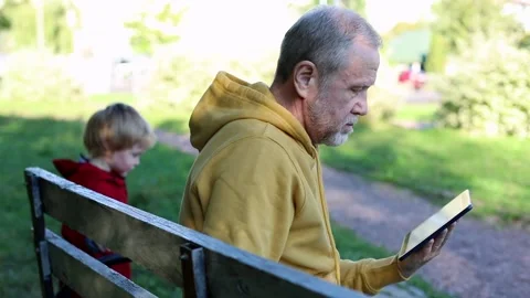 Smiling grandfather using digital tablet resting outside with cute blonde boy si Vídeos de archivo 142350874