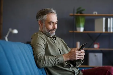 Smiling grey-haired man using mobile phone apps, texting message, browsing Foto stock