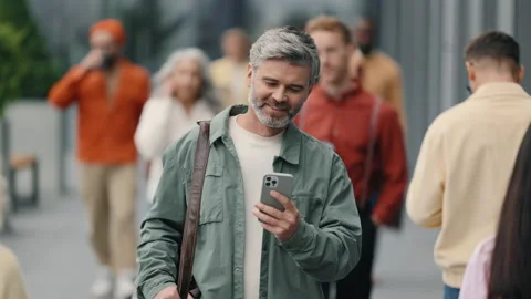 Smiling grey haired man walking in street and using mobile Stock Footage 167921985