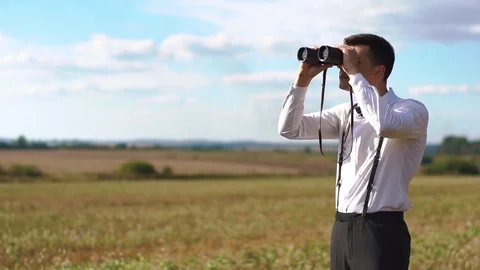 The smiling groom in the vintage suit is watching at the sky using binoculars at Stock Footage
