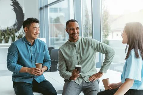 Smiling group of multiethnic colleagues drinking coffee and talking during break Stock Photos