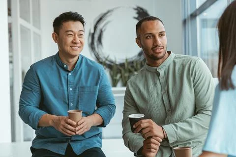 Smiling group of multiethnic colleagues drinking coffee and talking during break Stock Photos