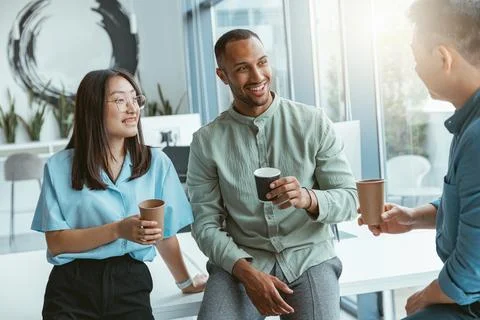 Smiling group of multiethnic colleagues drinking coffee and talking during break Stock Photos