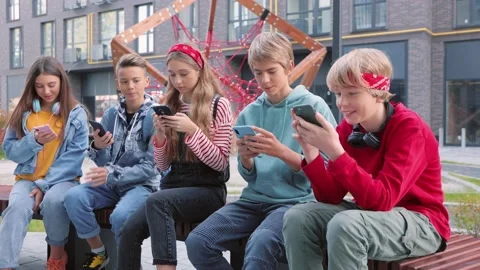 Smiling group of teens using gadgets sitting in row on bench. Happy boys and Video stock 200468195