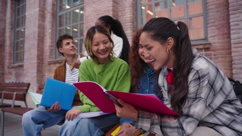 Smiling group of young students sitting on bench studying together outside Stock Footage 271602693