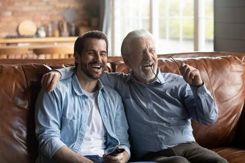 Smiling grownup son and old father watch TV together Stock Photos