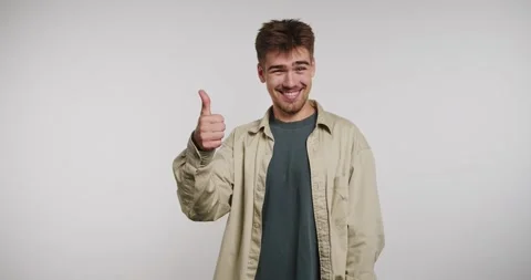 Smiling guy gives thumbs up expressing joy in a bright studio setting Vídeo Stock 329112894