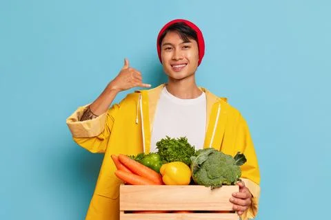 Smiling guy in red hat and yellow coat poses against blue background, box with Stock-Fotos