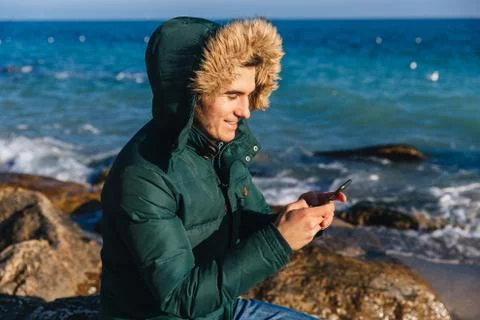 Smiling guy typing a message on smartphone by the sea. Stock Photos