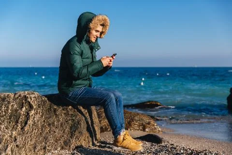 Smiling guy using his smartphone on the beach. Stock Photos
