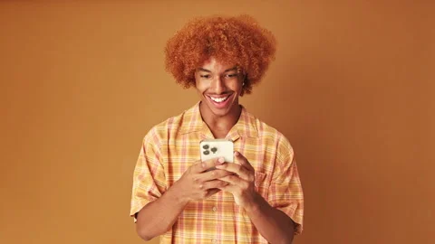 Smiling guy writing sms on mobile phone, isolated on brown background in studio Stock Footage 254914283