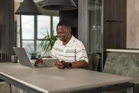 Smiling handsome african man using tablet with social networks at home, hap.. Stock Photos