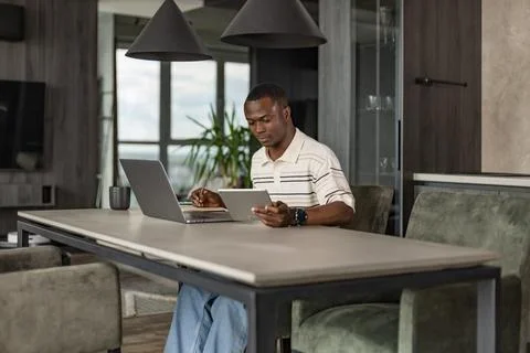 Smiling handsome african man using tablet with social networks at home, hap.. Foto stock