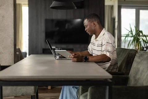 Smiling handsome african man using tablet with social networks at home, hap.. Stock Photos