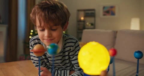 Smiling handsome boy looking at children's model of solar system. He is wearing Vídeo Stock 210493150