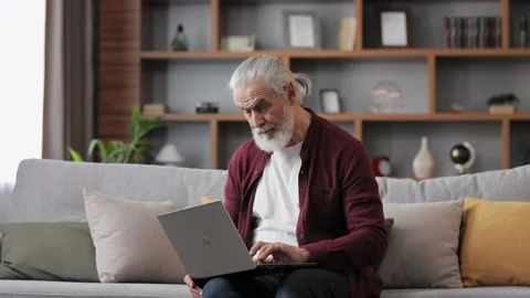 Smiling handsome elderly gray-haired man working with laptop sitting on the Stock Footage 200254236