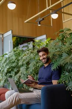 Smiling handsome freelancer is making notes during work on laptop in coworking Stock Photos