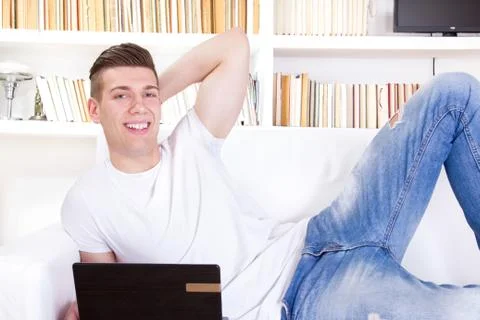 Smiling handsome guy lying on sofa using laptop computer Stock Photos
