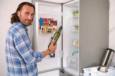 Smiling handsome man looking at camera, holding a dark glass bottle with or.. Stock Photos