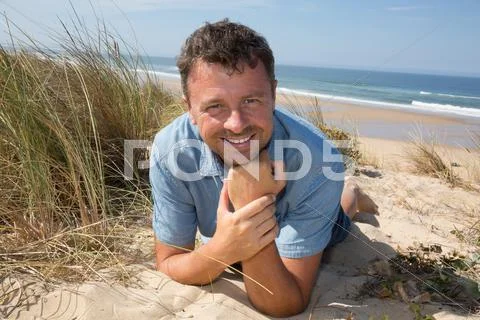 Smiling handsome man relaxing on the beach lying on sand Stock Photos