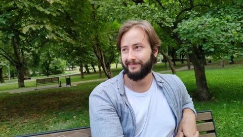 Smiling handsome man is sitting on bench in city public park on summer day Stock Footage 221192256