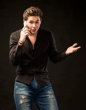 Smiling handsome man with smartphone talking over black background 写真素材