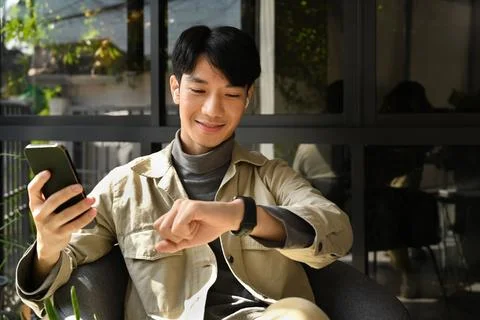 Smiling handsome man using smart phone and checking arrival time on his watch Stock Photos