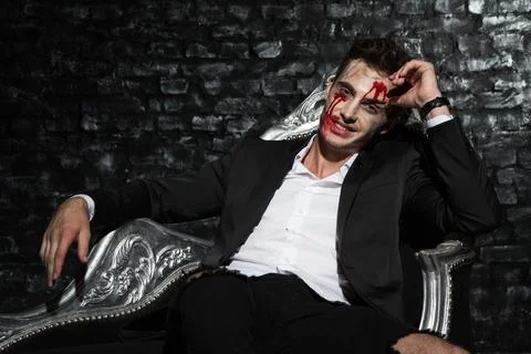 Smiling handsome vampire chilling on silver couch Stock Photos
