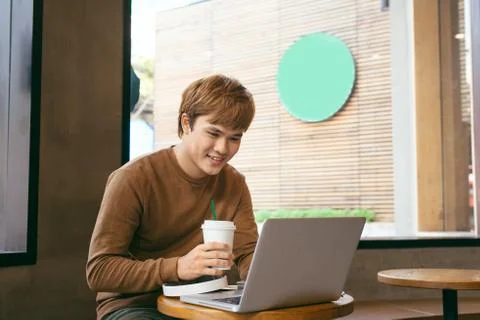 Smiling handsome worker in glasses drinking coffee while watching video on hi Stock Photos