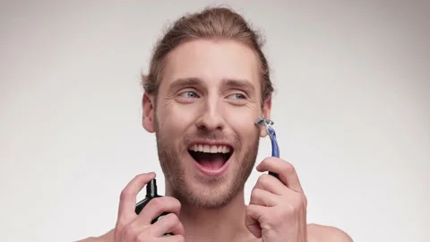 Smiling handsome young man with razor and perfumes in hand on white background Stock Footage 164322455