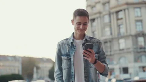 Smiling handsome young man use phone stand at old city street. Happy at sunlight Stock Footage 146758460