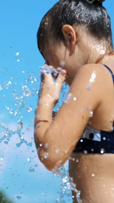 Smiling, happy eight year old girl in swimsuit having fun in splashes in street Stock Footage 313865176