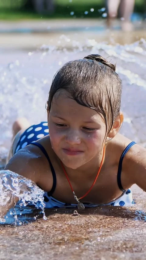 Smiling, happy eight year old girl in swimsuit having fun in splashes in street Stock Footage 315219623